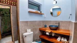 Ein Badezimmer mit Toilette, einer Holzablage mit Waschbecken, einem Spiegel und einem Fenster über der Ablage.