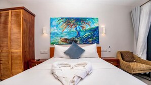Ein Hotelzimmer mit einem Bett, einem Gemälde von Baum und Boot, einem herzförmigen Handtuch, einem Holzschrank und einem Korbstuhl.