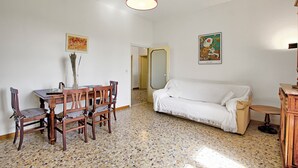 Una habitación con una mesa de comedor, sillas, un sofá blanco y una lámpara colgante roja.