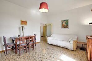 A room with a dining table, chairs, a white sofa, and a red hanging light fixture.
