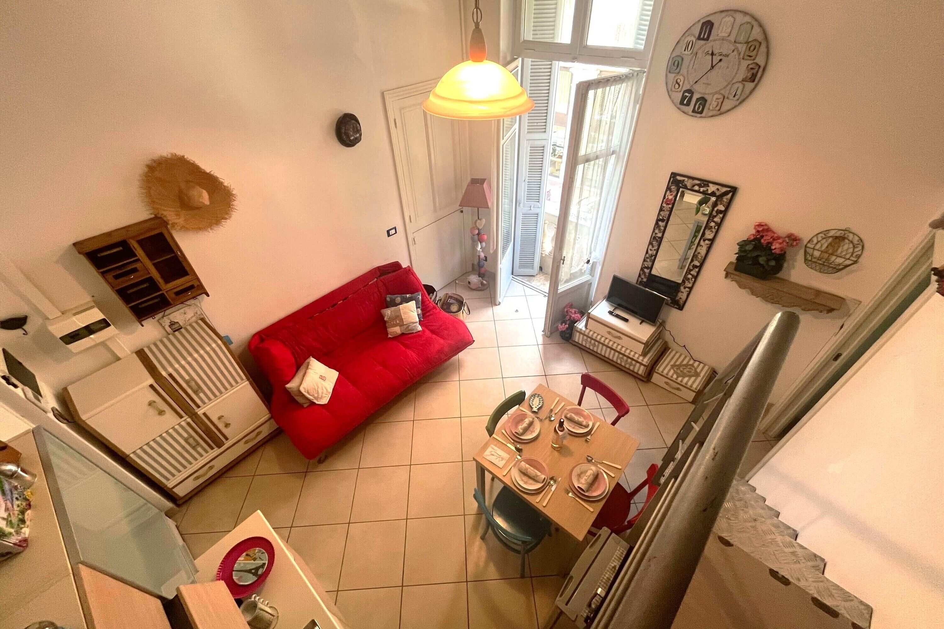 Un espacio habitable compacto con un sofá rojo, una mesa de comedor dispuesta para cuatro personas y una escalera que sube a un piso superior.
