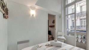 A hotel room with a bed, a window with a view of buildings, a wall-mounted light, and a radiator.