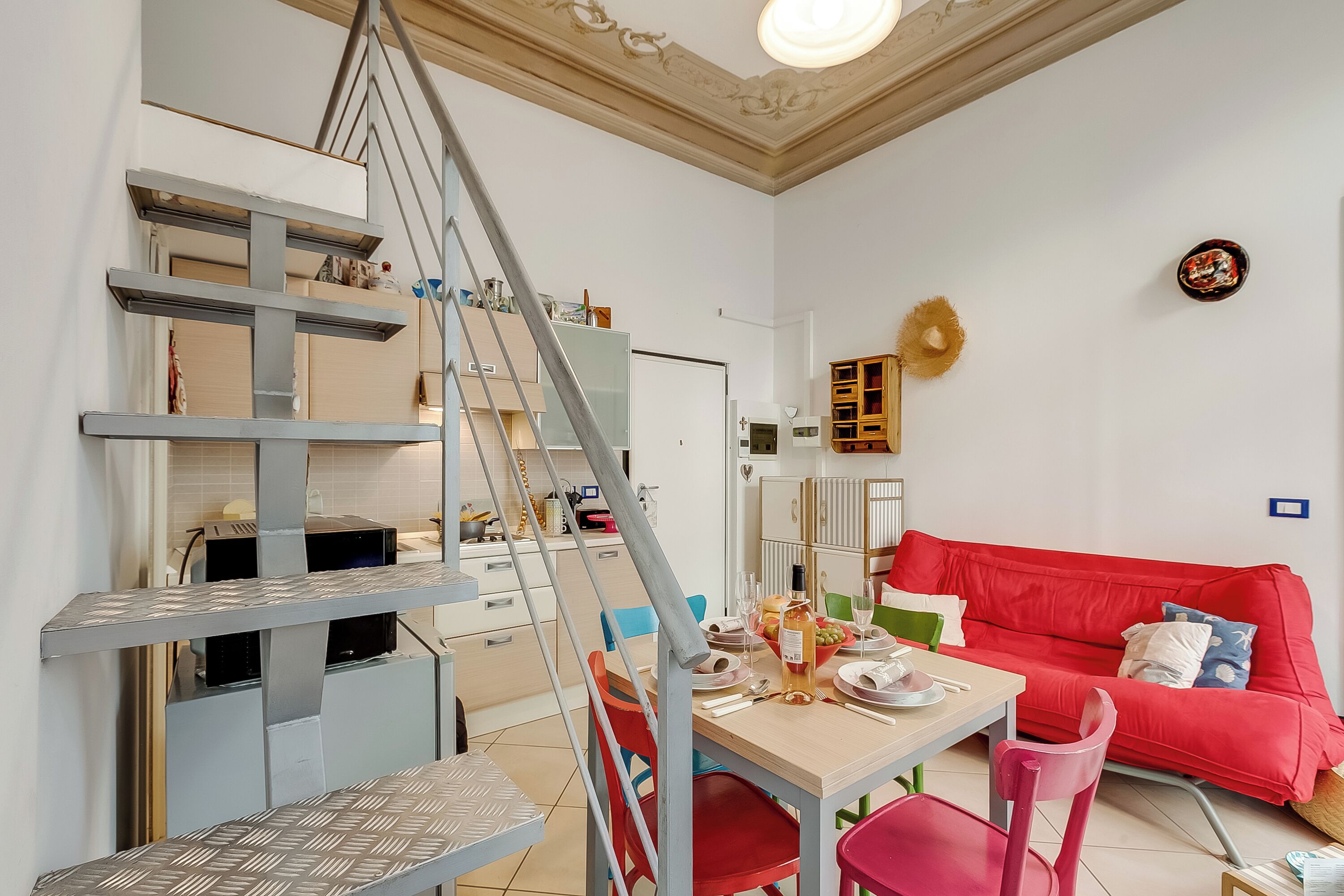 Ein modernes Wohnzimmer mit Treppe, einem roten Sofa und einem Essbereich mit Tisch für zwei Personen.