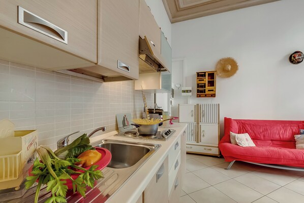 Une cuisine moderne équipée d’un évier, d’une cuisinière et de placards. On aperçoit un canapé rouge et un élément décoratif mural à l’arrière-plan.