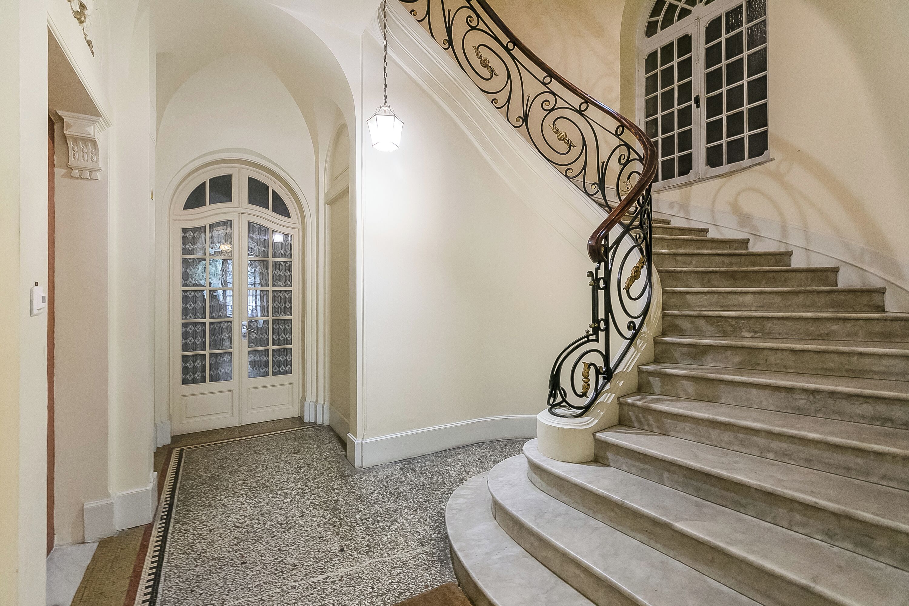 A grand staircase with ornate metal railings and a carpeted floor leading to a door with glass panels.