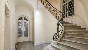 A grand staircase with ornate metal railings and a carpeted floor leading to a door with glass panels.