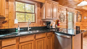 Cocina de cabaña de madera con encimera de granito, armarios de madera y pileta de acero inoxidable.