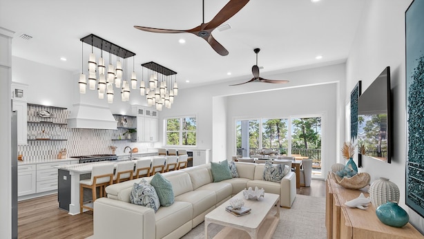 A spacious living area with a large L-shaped sofa, a coffee table, and a dining area with chairs. There is a kitchen with white cabinets and a stove, and a ceiling fan above. - Villa Rosa - Coastal Home Complete with Private Pool and Outdoor Dining (Santa Rosa Beach)
