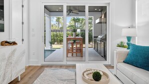 A modern living room with a sliding glass door leading to an outdoor patio area. - Villa Rosa - Coastal Home Complete with Private Pool and Outdoor Dining (Santa Rosa Beach)