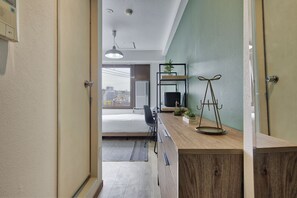 A modern hotel room with a wooden desk, a black chair, a bed, and a view of the city through the window. - Modern Living Tokyo Komagome 502, a compact studio at excellent location (豊島区駒込1丁目30-6)