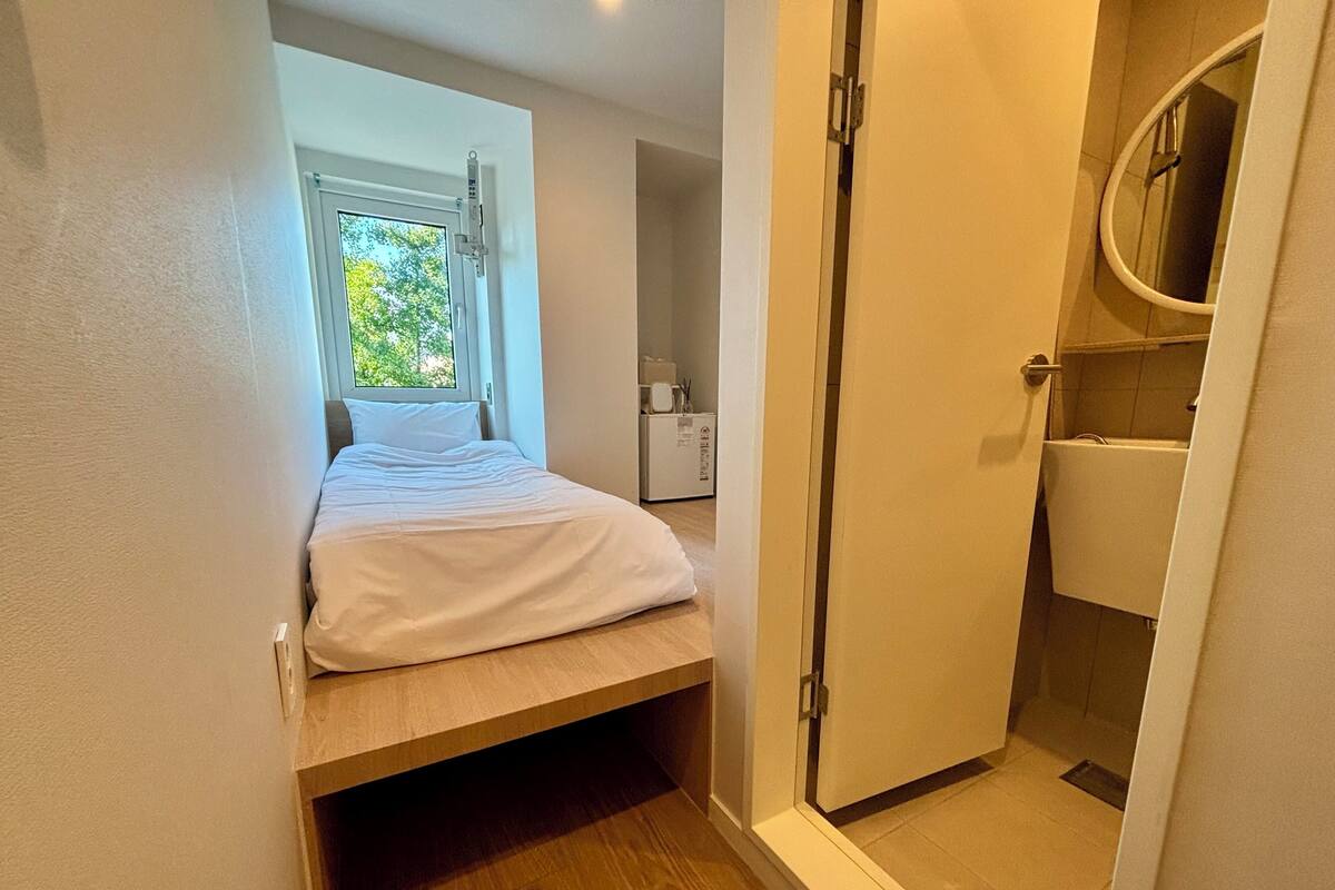 A compact bedroom with a bed, a small window, and a shower area.