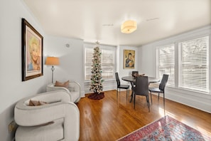 Ein modernes Wohnzimmer mit Weihnachtsbaum, einem Essbereich mit Tisch und Stühlen sowie einem großen Fenster mit Jalousien.