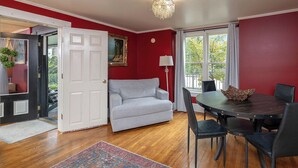 A room with a red wall, a white door, a grey sofa, a dining table with black chairs, and a chandelier. - Eureka Springs 3 Bed - Teacup Cottage (Eureka Springs)