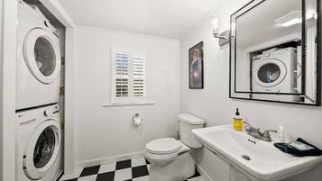 Un baño con piso a cuadros, un inodoro, un lavamanos y dos lavadoras.