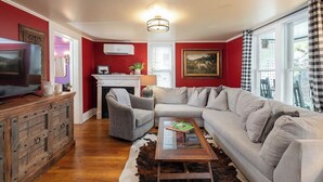 A living room with a sofa, armchair, wooden cabinet, and a television. - Eureka Springs 3 Bed - Teacup Cottage (Eureka Springs)