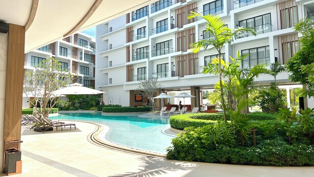 A modern hotel with a swimming pool, lounge chairs, and greenery. - 1BR 5Min Walk to BeachPool&Gym C243 (Choeng Thale)