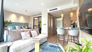 A modern hotel room with a sofa, a small table, a kitchen area with bar stools, and a bathroom visible through an open door. - 1BR 5Min Walk to BeachPool&Gym C243 (Choeng Thale)