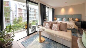 A modern hotel room with a large bed, a sofa, a small table, and a view of the city through large windows. - 1BR 5Min Walk to BeachPool&Gym C243 (Choeng Thale)