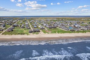 A coastal residential area with houses arranged in rows along the beach, featuring a clear view of the ocean and a distant shoreline.