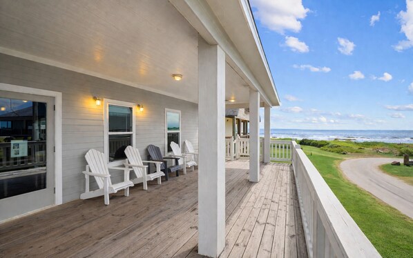 A wooden deck with white chairs, a covered area with a railing, and a view of the ocean.