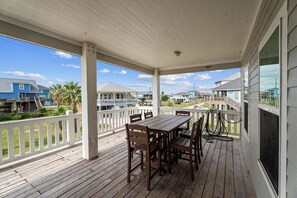 A covered porch with a wooden table and chairs, white railings, and a view of neighboring houses.