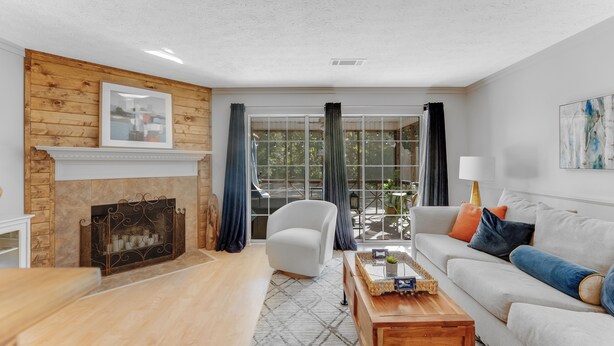 A living room with a fireplace, a sofa, a coffee table, and a view through large windows. - Lake Martin Condo-charming near Auburn-Dadeville in Stillwater (Dadeville)