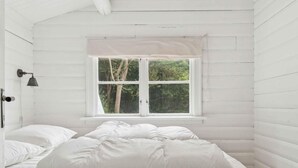 Une pièce en bois peinte en blanc, avec un lit, une fenêtre et une lampe fixée au mur.