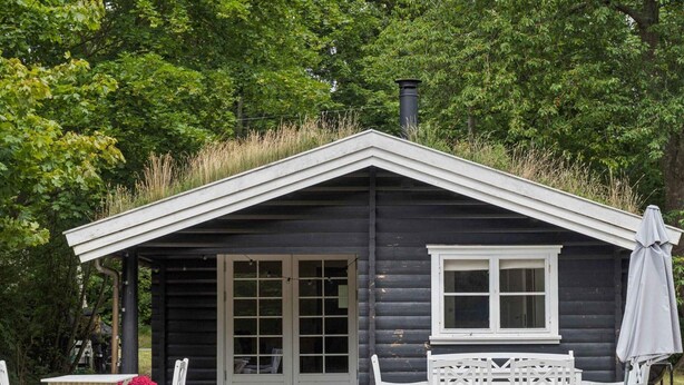 Une petite cabane avec un toit en pente, une fenêtre et une table avec des chaises à l’extérieur.
