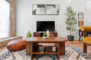 Un salon avec un mur en pierre, un téléviseur à écran plat, une table basse en bois, une plante en pot et un canapé.