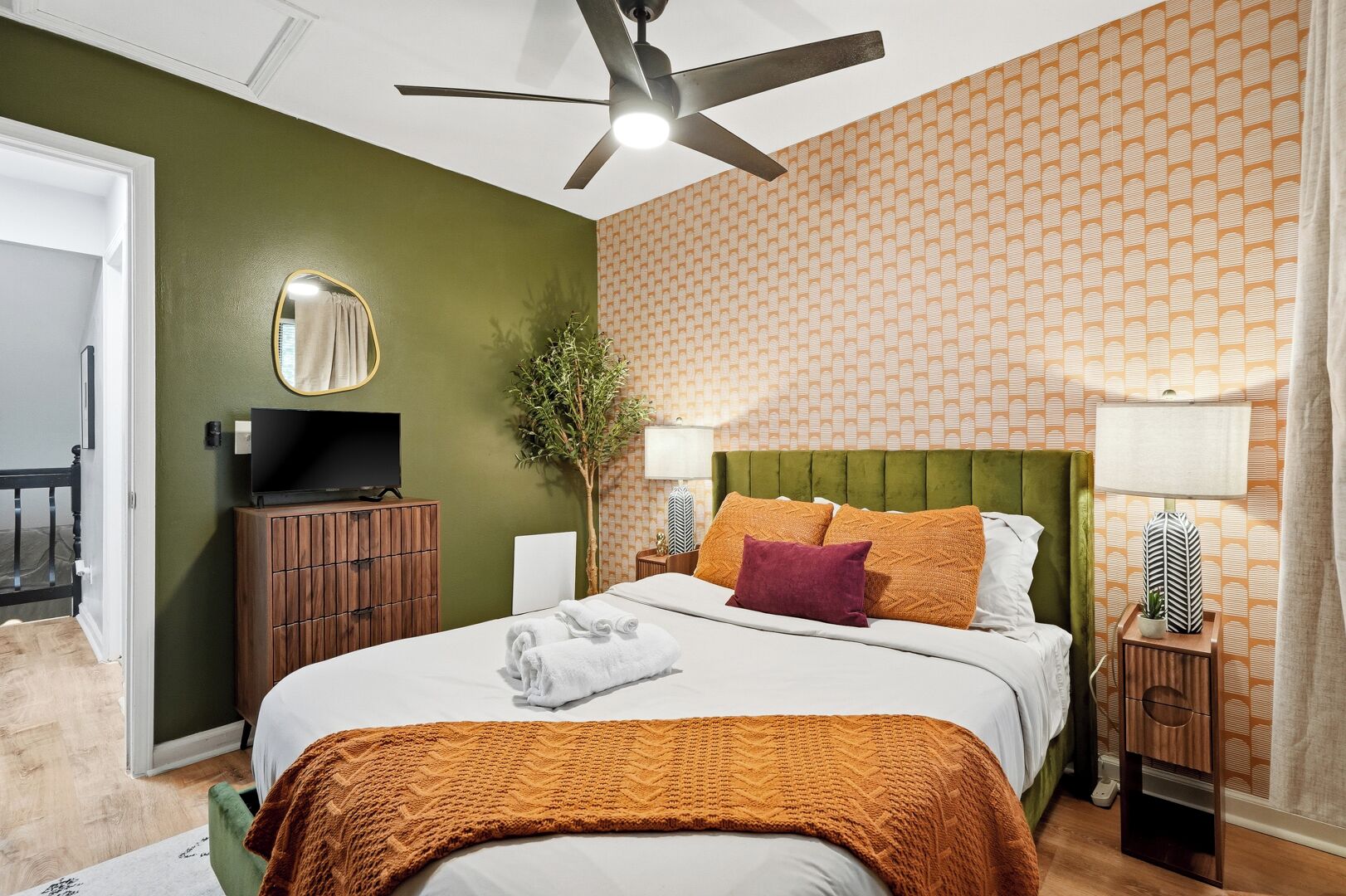 A hotel room with a bed, a television, a green headboard, and a patterned wall.