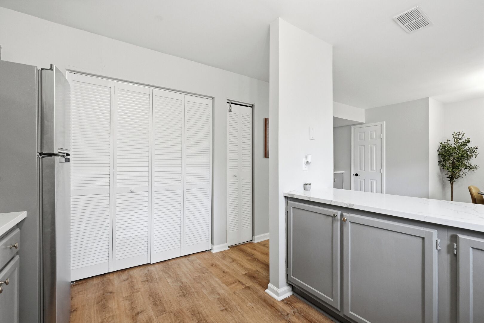 A kitchen with grey cabinets, a white countertop, and a wooden floor.