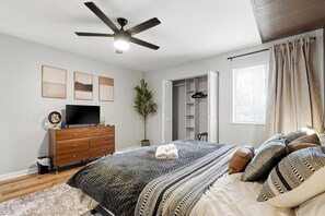 A bedroom with a bed, a dresser, a television, a ceiling fan, and a window with curtains.