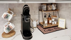 Eine Kaffeestation mit einer Keurig-Kaffeemaschine, einem Becherhalter, einer Ablage mit Kaffeetassen und einem gerahmten Schild.