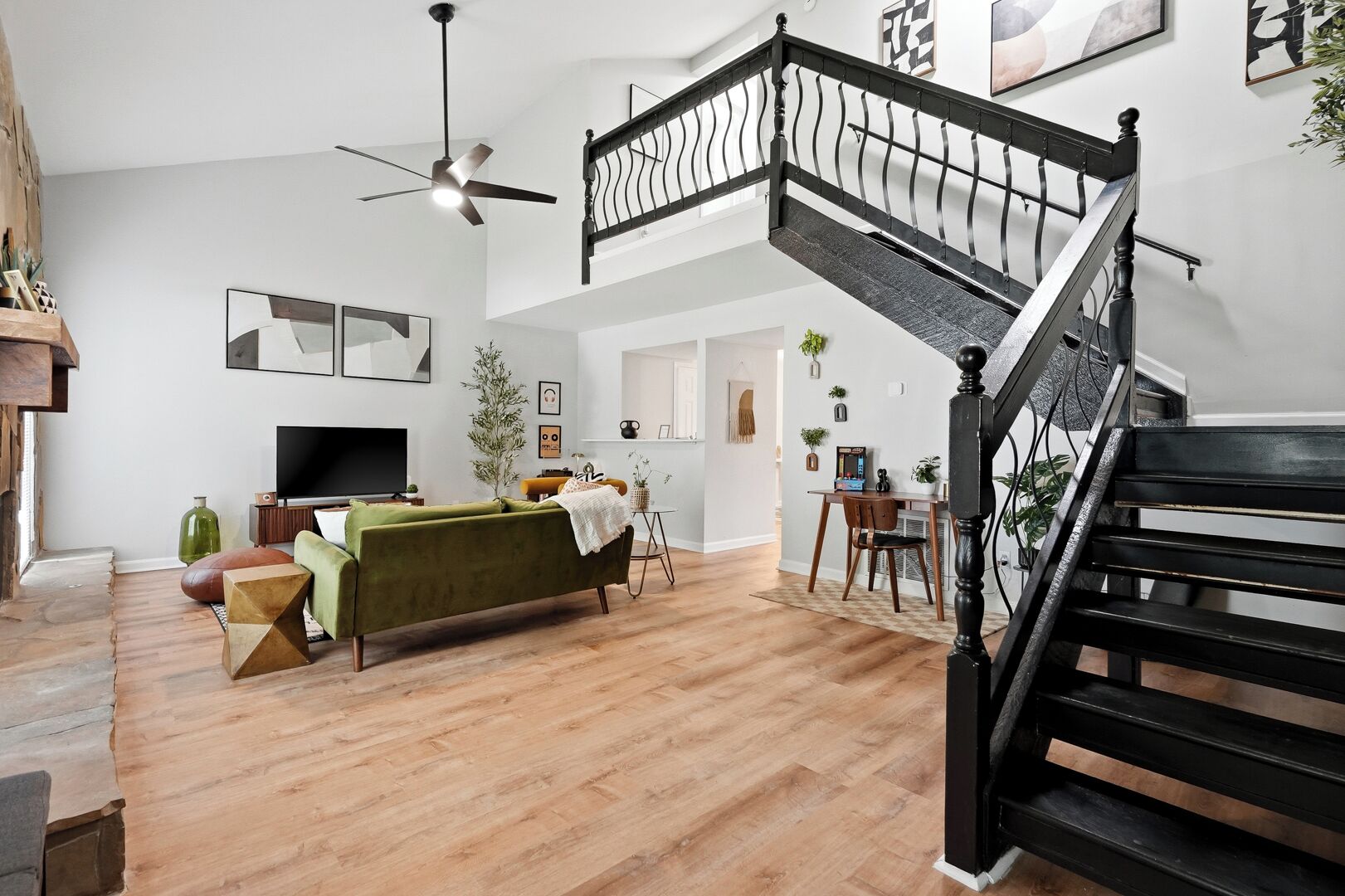 A spacious living area with a green sofa, wooden flooring, a black staircase, and a ceiling fan.