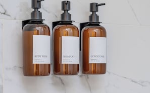 Three bottles of body wash, shampoo, and conditioner with pump dispensers, labeled as essentials, each containing 21 FL OZ / 621 ML. - Heritage Haus: Stylish 2BR Near Marietta Square / Dogs Ok / Parking + WFH Ready (Marietta)