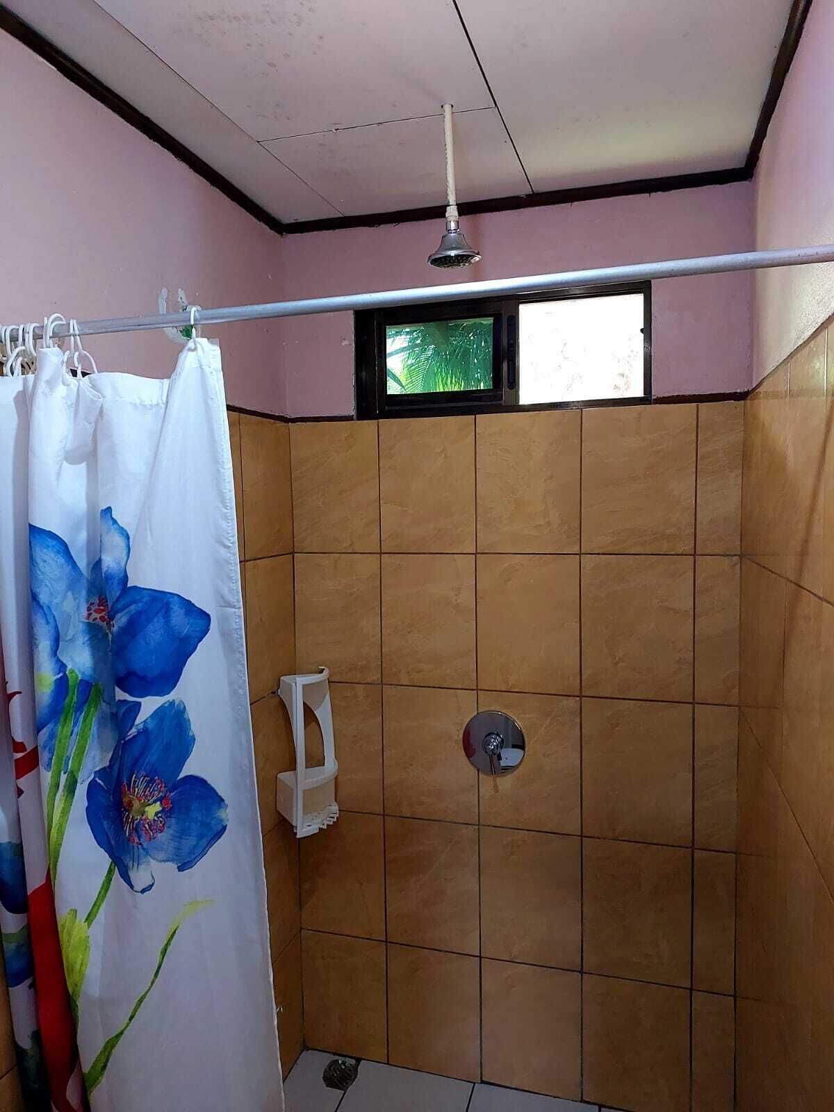 Área de chuveiro com parede revestida de azulejos, chuveiro e uma janela acima.