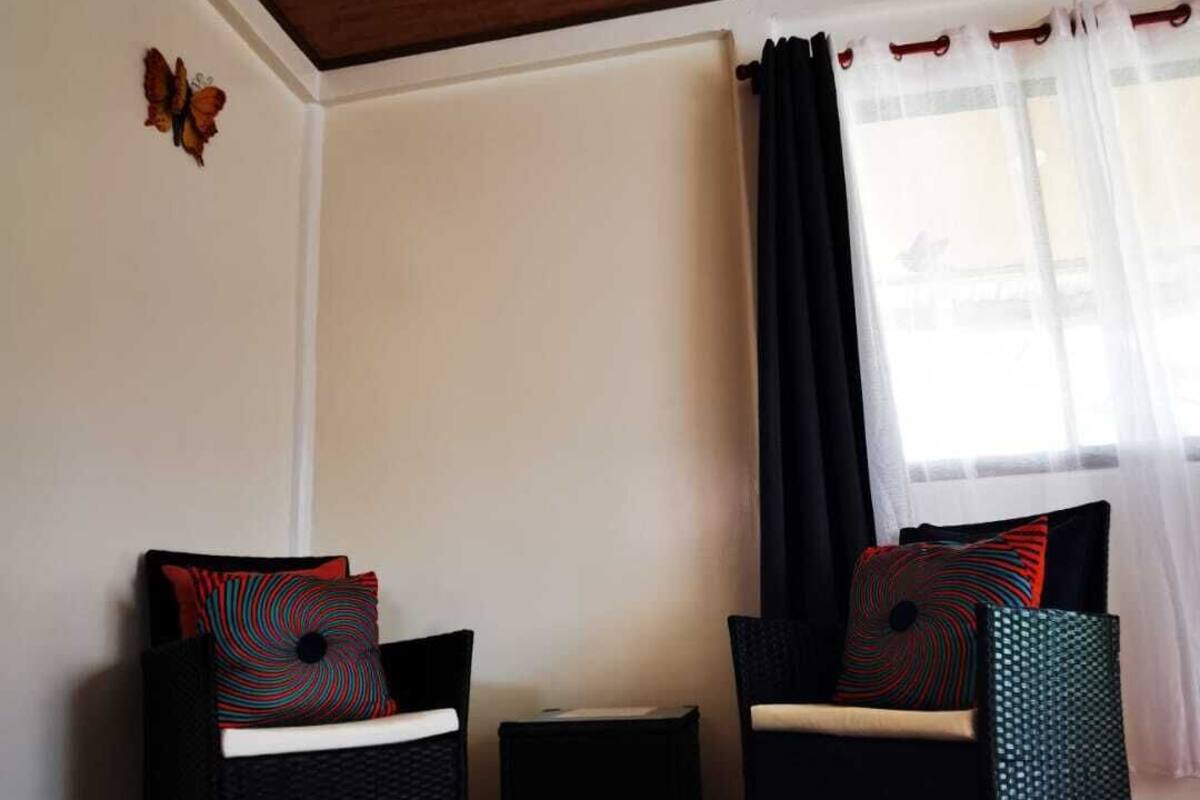 A room with two wicker chairs, a small table, and a black rug on a wooden floor.