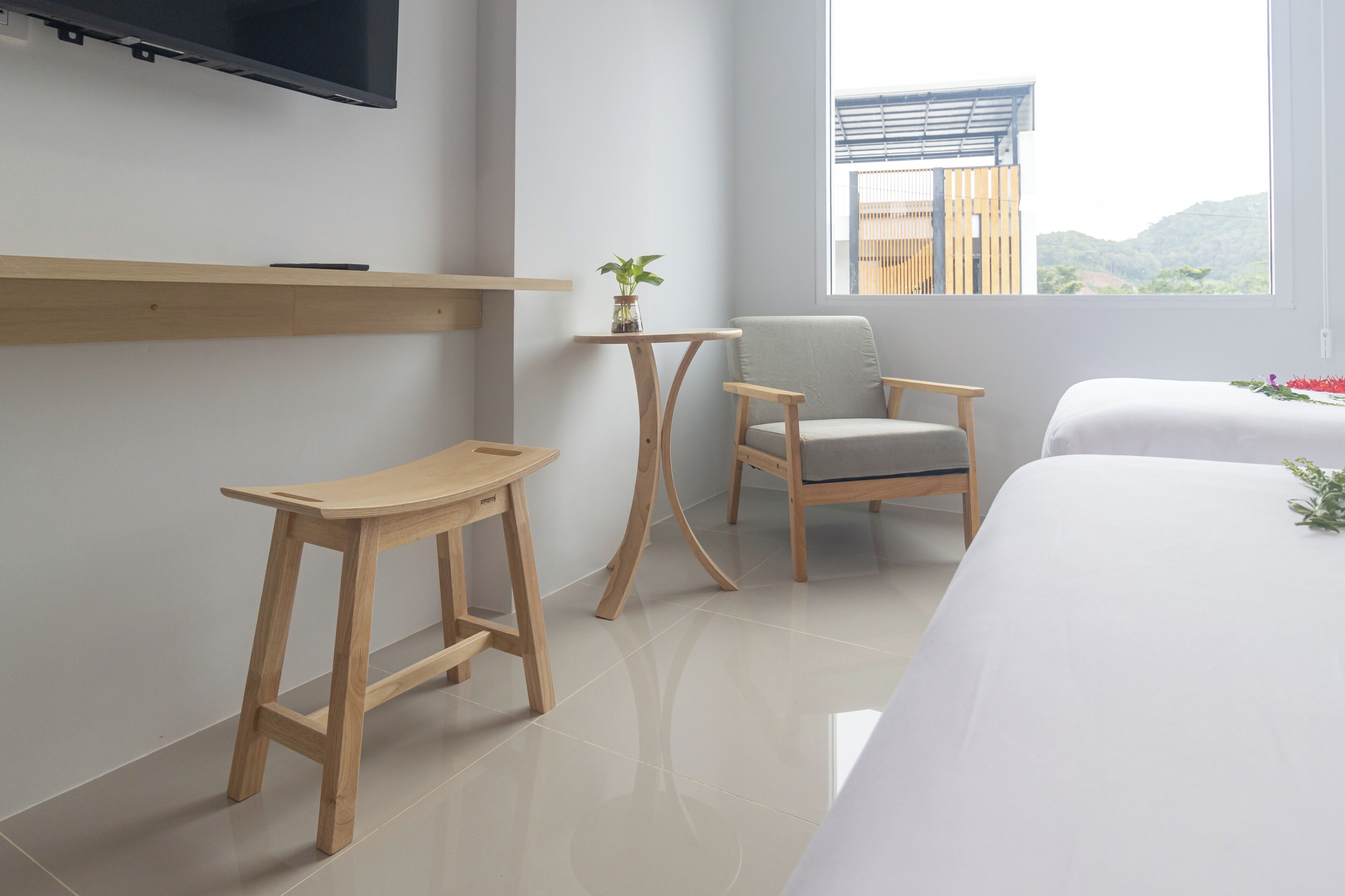 A modern hotel room with a large bed, a small wooden table, a chair, a TV mounted on the wall, and a window with a view of the outdoors.