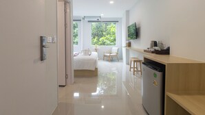 Una habitación de hotel moderna con una cama, una mesita, una silla, un televisor y un refrigerador.