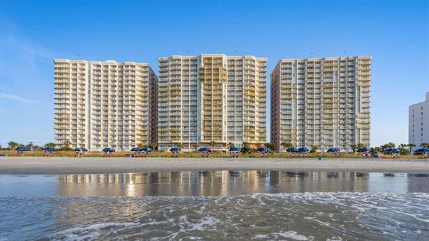 A beachfront hotel with multiple high-rise buildings, a sandy beach, and umbrellas.