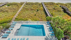 A pool area with a clear view of the ocean, surrounded by a wooden deck and lounge chairs. - Panoramic Ocean View Condo with Pool (North Myrtle Beach)