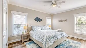 Une chambre à coucher comprenant un lit, des tables de chevet, un ventilateur de plafond et des décorations murales représentant des poissons.