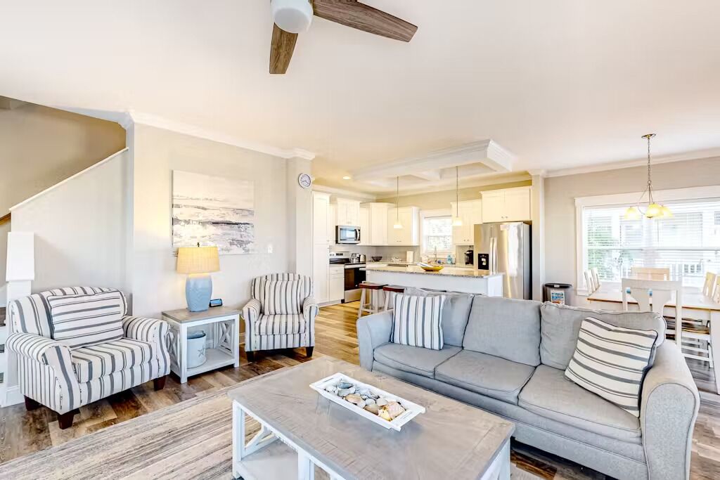 A spacious living room with a grey sofa, striped armchairs, a coffee table, and a staircase.