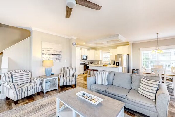 A spacious living room with a grey sofa, striped armchairs, a coffee table, and a staircase.