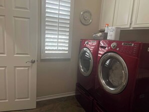 A laundry room with a red washer and dryer, a white door, and a window with blinds.