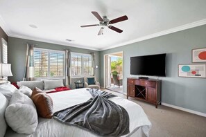 A bedroom with a bed, a television, a ceiling fan, and a view of the outdoors.