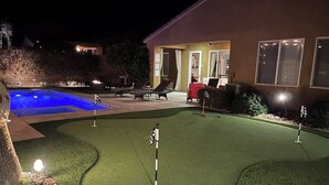 En nattbild av en golfbana med en puttinggreen, en pool och en byggnad med en uteplats.