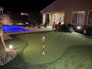 Ein Nachtblick auf einen Golfplatz mit Putting Green, Pool und einem Gebäude mit einer Terrasse.