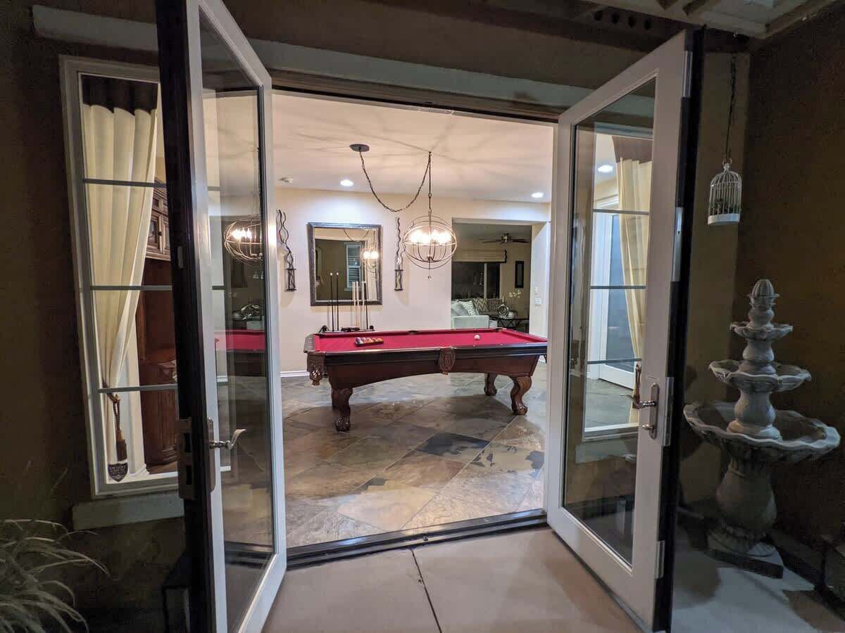 Una puerta abierta que da a un cuarto con mesa de billar, candelabro y fuente.