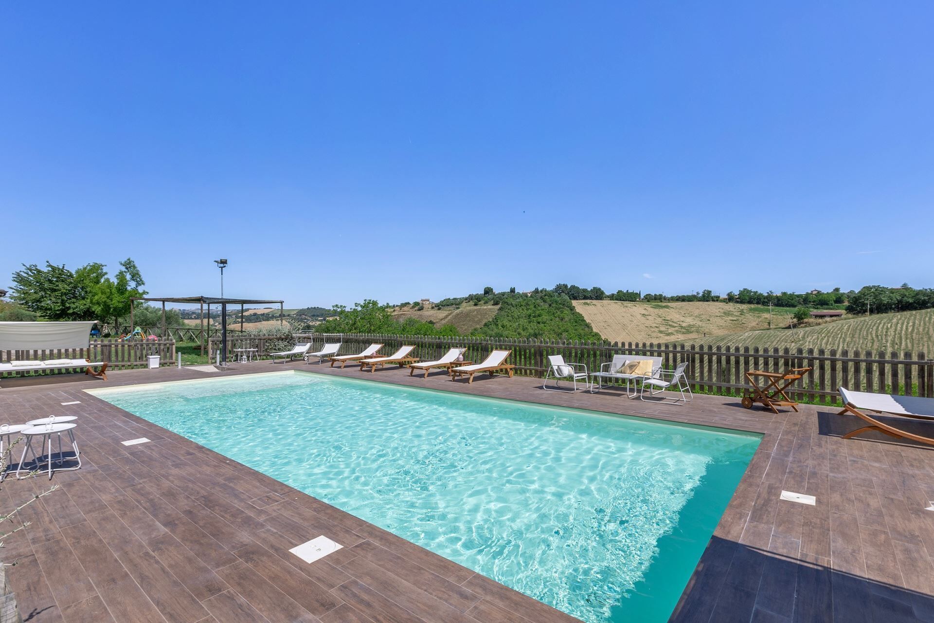 Una piscina rectangular con agua azul cristalina, rodeada de un suelo de madera.